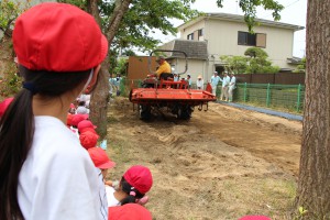 畑を耕すトラクターを見学する児童